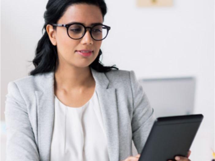 A picture of a woman with glasses looking at a tablet.