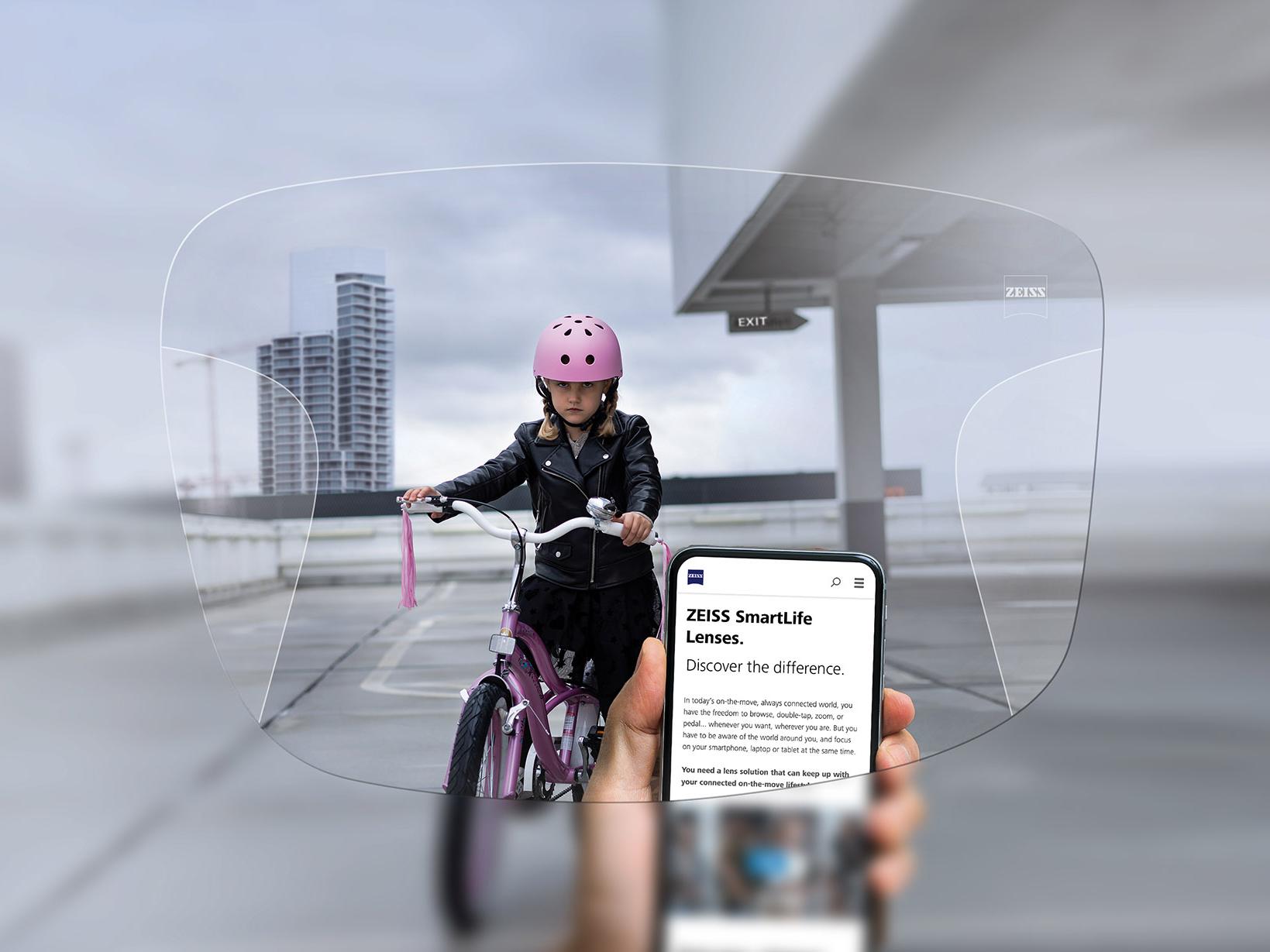 Person looking at his phone through ZEISS SmartLife Progressive lenses. In the background you can see a girl on her bike wearing a pink crash helmet. 