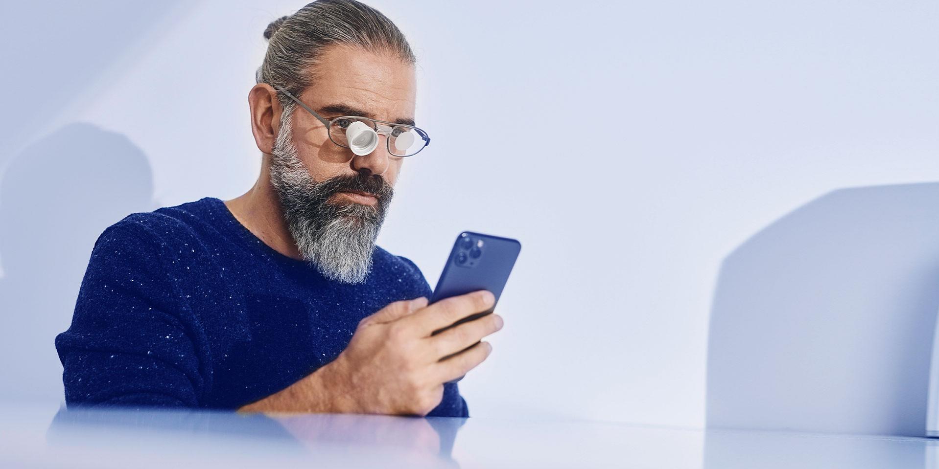 A man checks mobil phone and wears eye glasses with an inetgrated loupe.