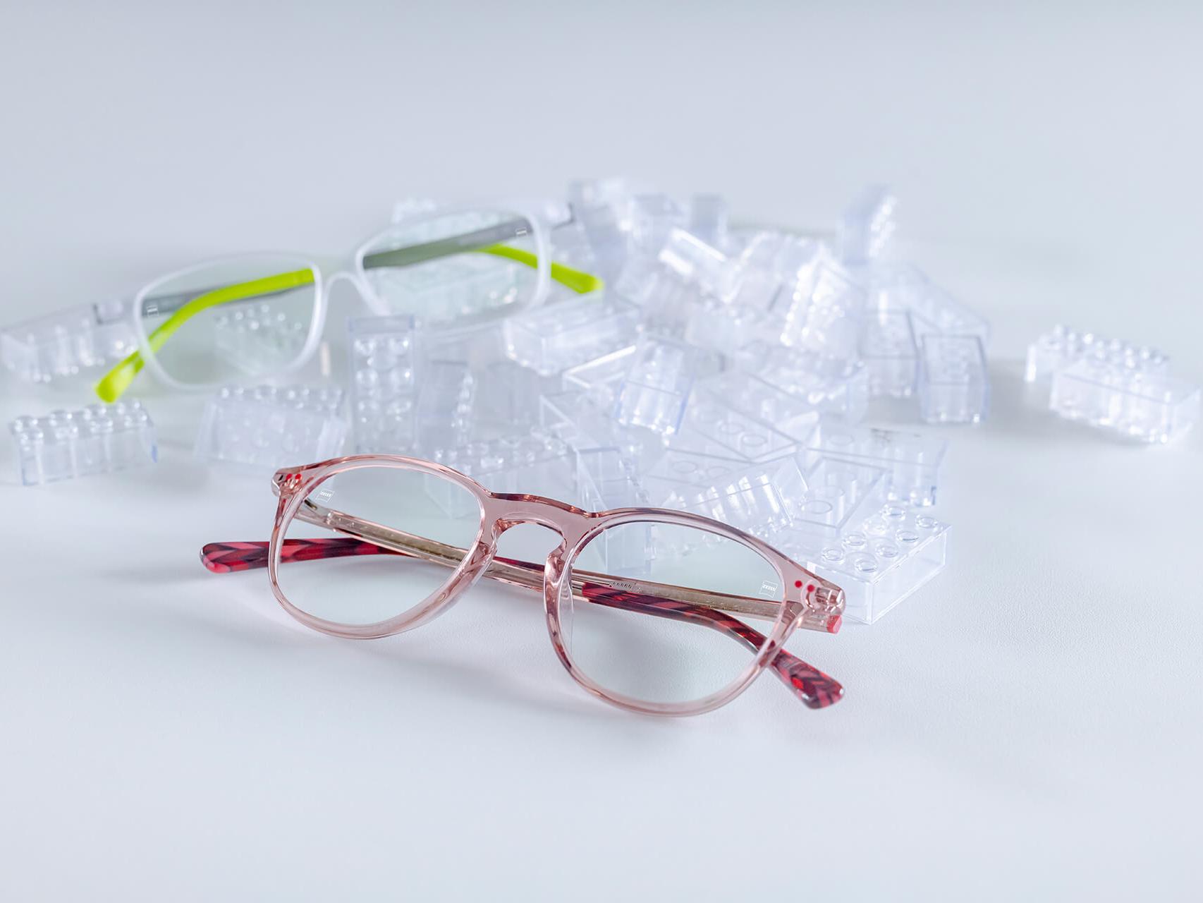 Two pairs of children's glasses with ZEISS lenses and DuraVision® kids coatings. The glasses are placed between transparent children's bricks.