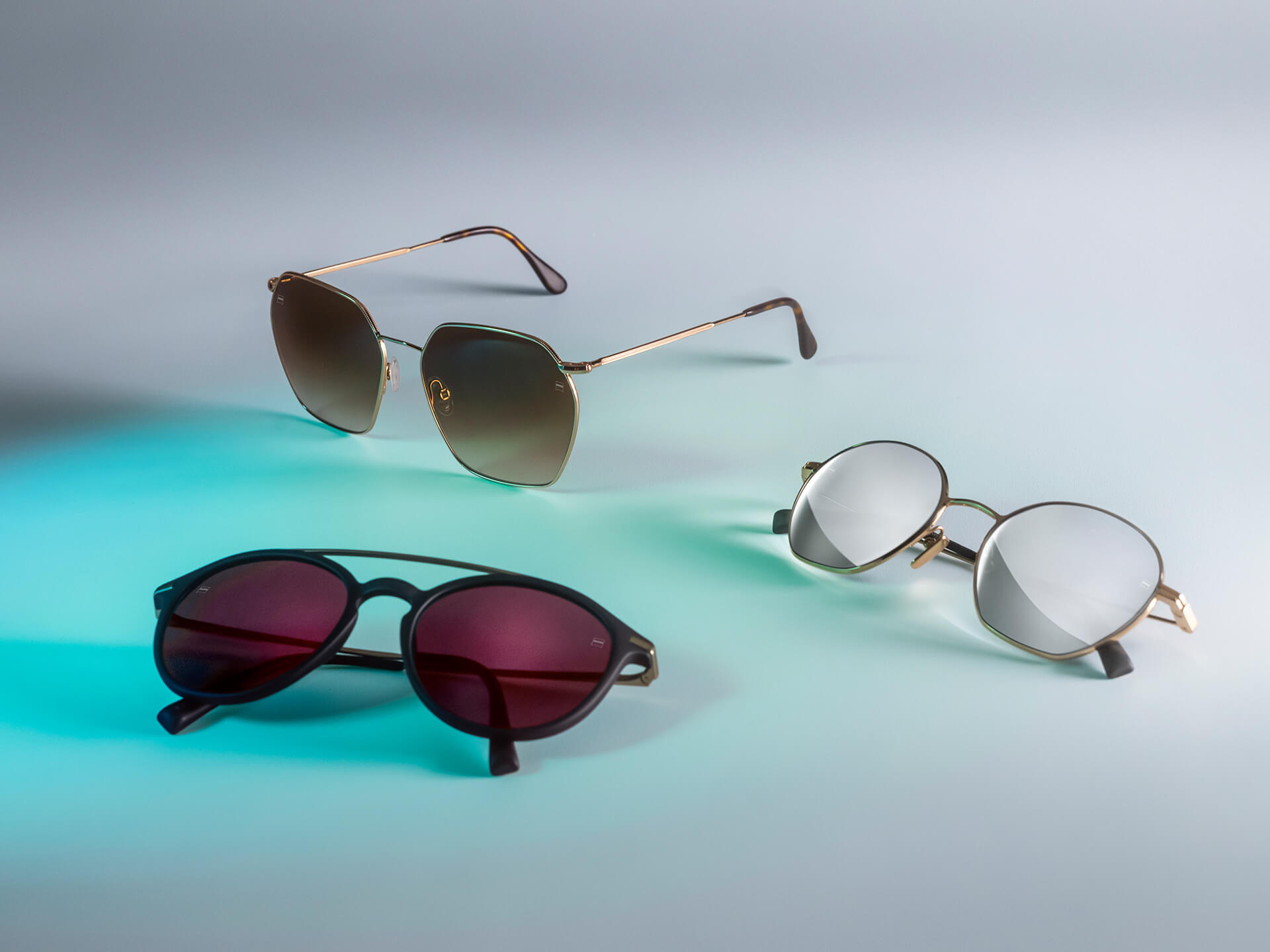 Three pairs of sunglasses with different coloured ZEISS sunglass lenses, featuring DuraVision Sun, DuraVision Mirror, and Flash Mirror coatings, visible on a white background with blue light reflection.